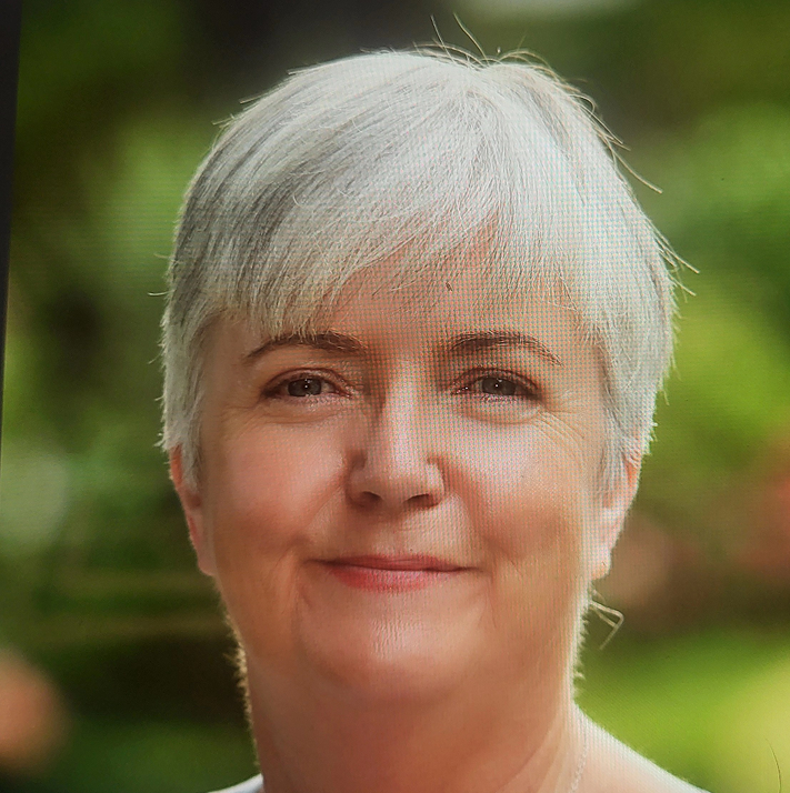 A smiling older woman with short grey hair stands outdoors, with a blurred green background suggesting a garden or park setting—her warm presence reflecting the supportive spirit of Galways Sick Kids.