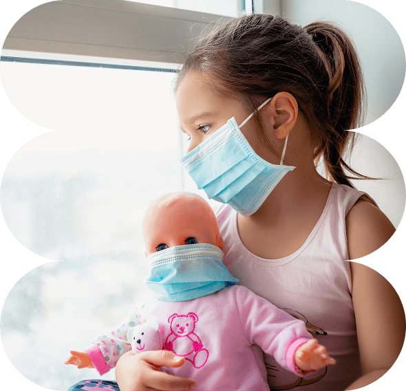 A young girl wearing a face mask looks out of a window while holding a doll that is also wearing a mask. Both appear indoors in a softly lit room, capturing the quiet resilience of Galway's Sick Kids during challenging times.