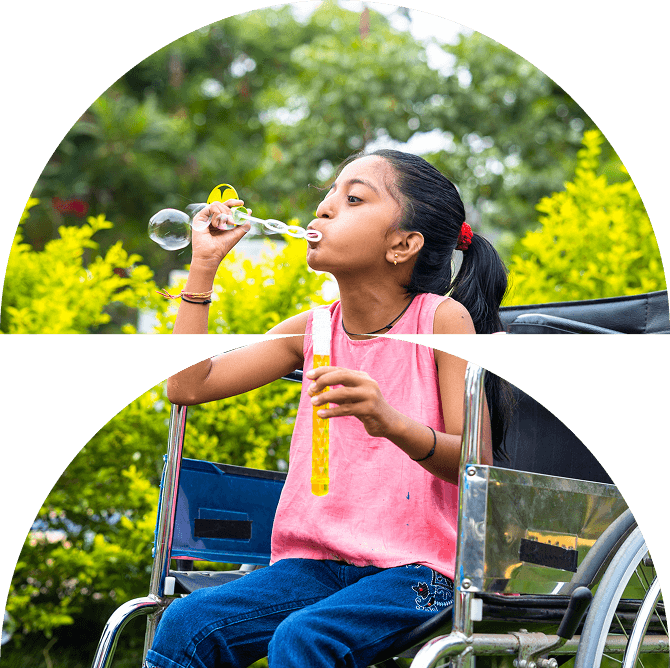 A young girl from Galway’s Sick Kids in a wheelchair outdoors, wearing a pink top and jeans, blows bubbles with a bubble wand, surrounded by green bushes.