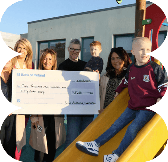 A group of adults and children stand by a playground slide, holding a large charity cheque for €5,250 from Bank of Ireland to Galway’s Sick Kids. One child sits smiling at the top of the slide.
